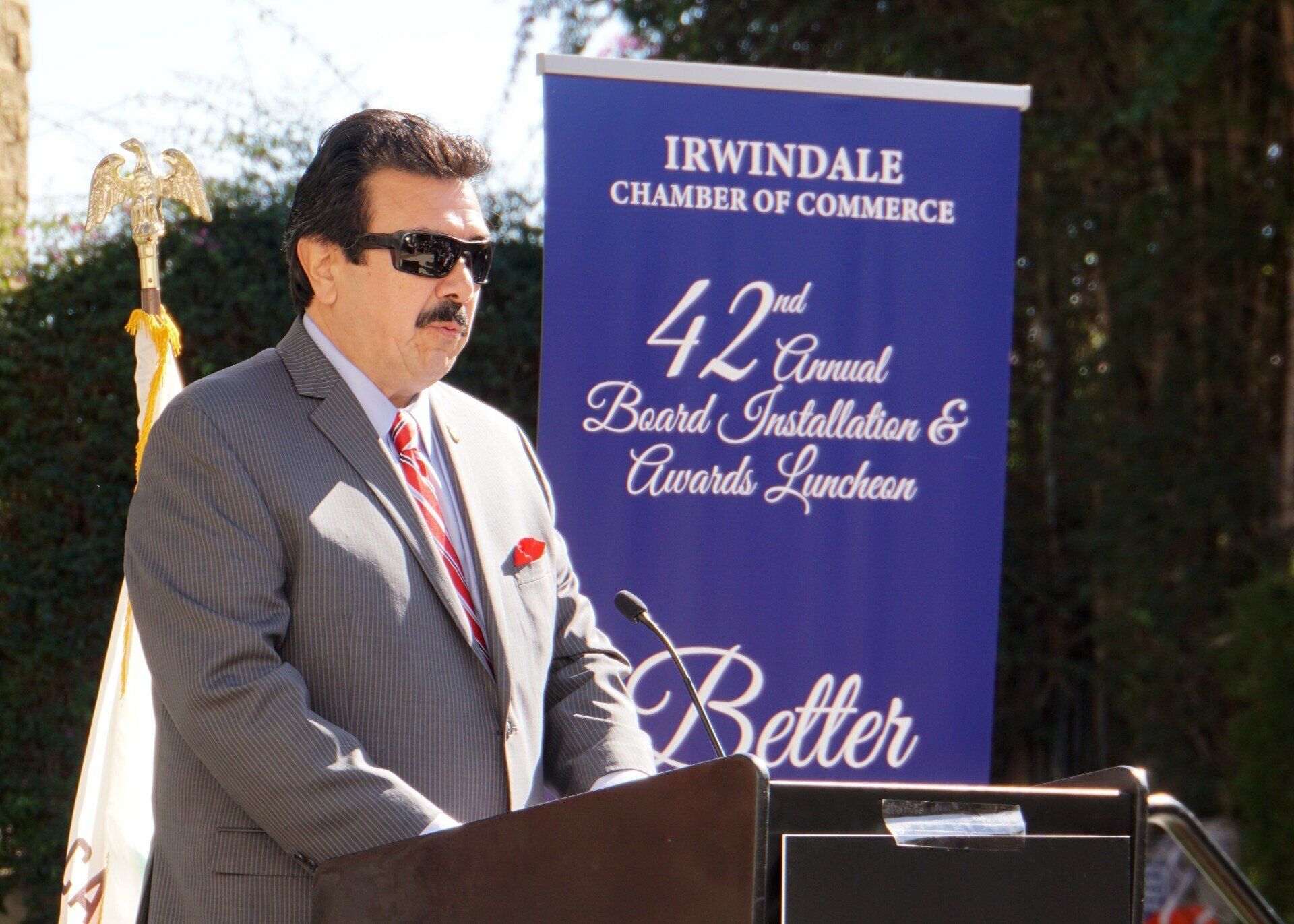 A man stands at a podium in front of a sign that says irwindale chamber of commerce