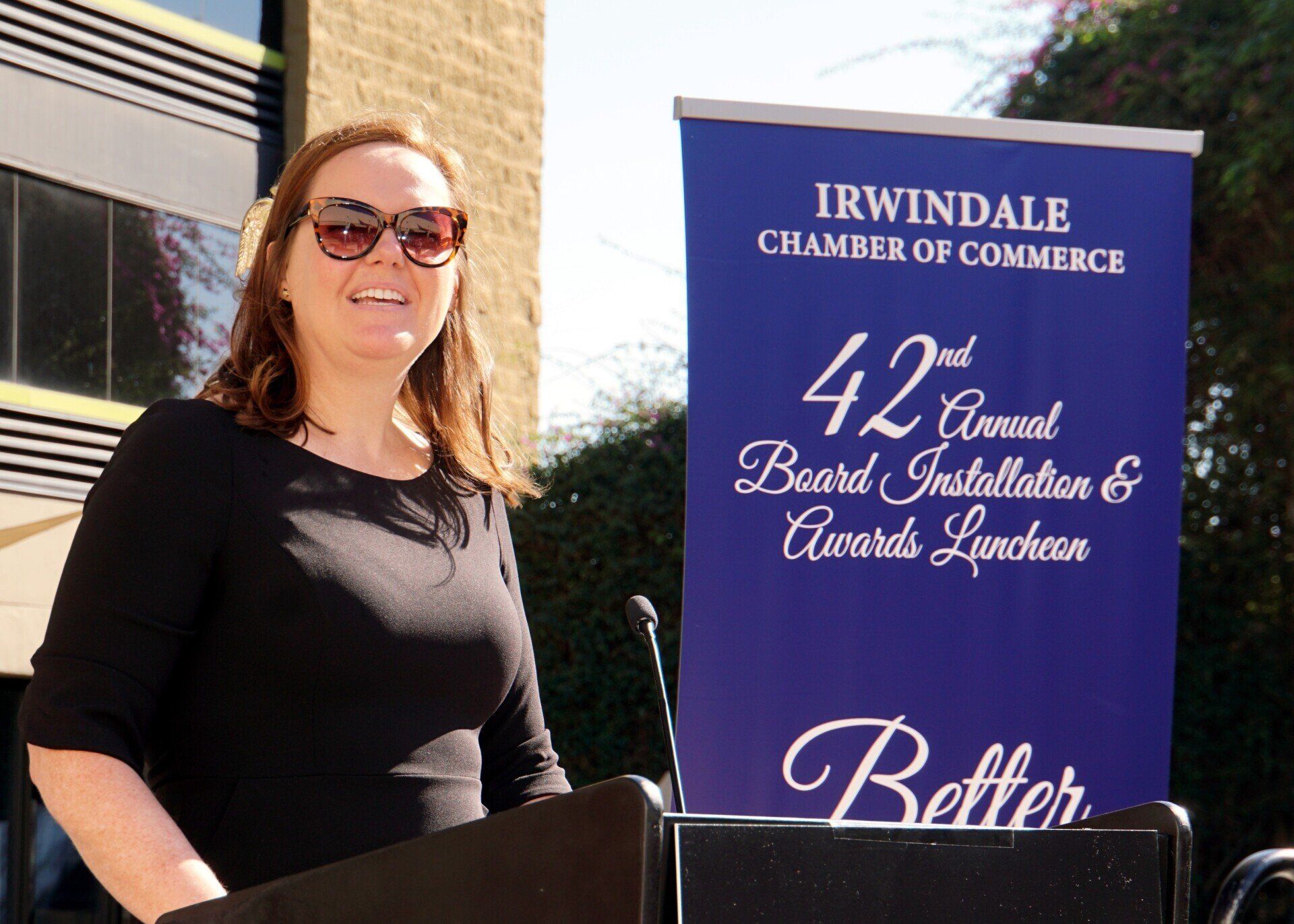 A woman stands at a podium in front of a sign that says irwindale chamber of commerce