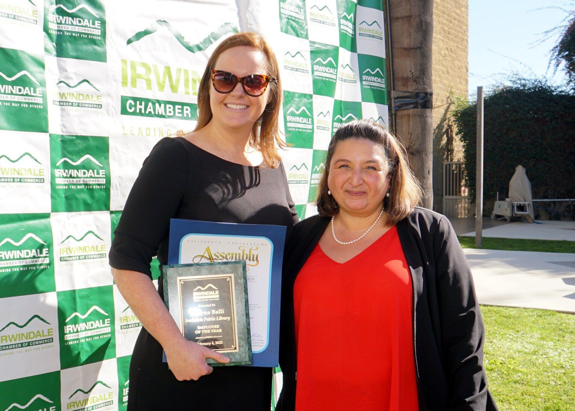 Two women are posing for a picture in front of a green and white checkered backdrop.