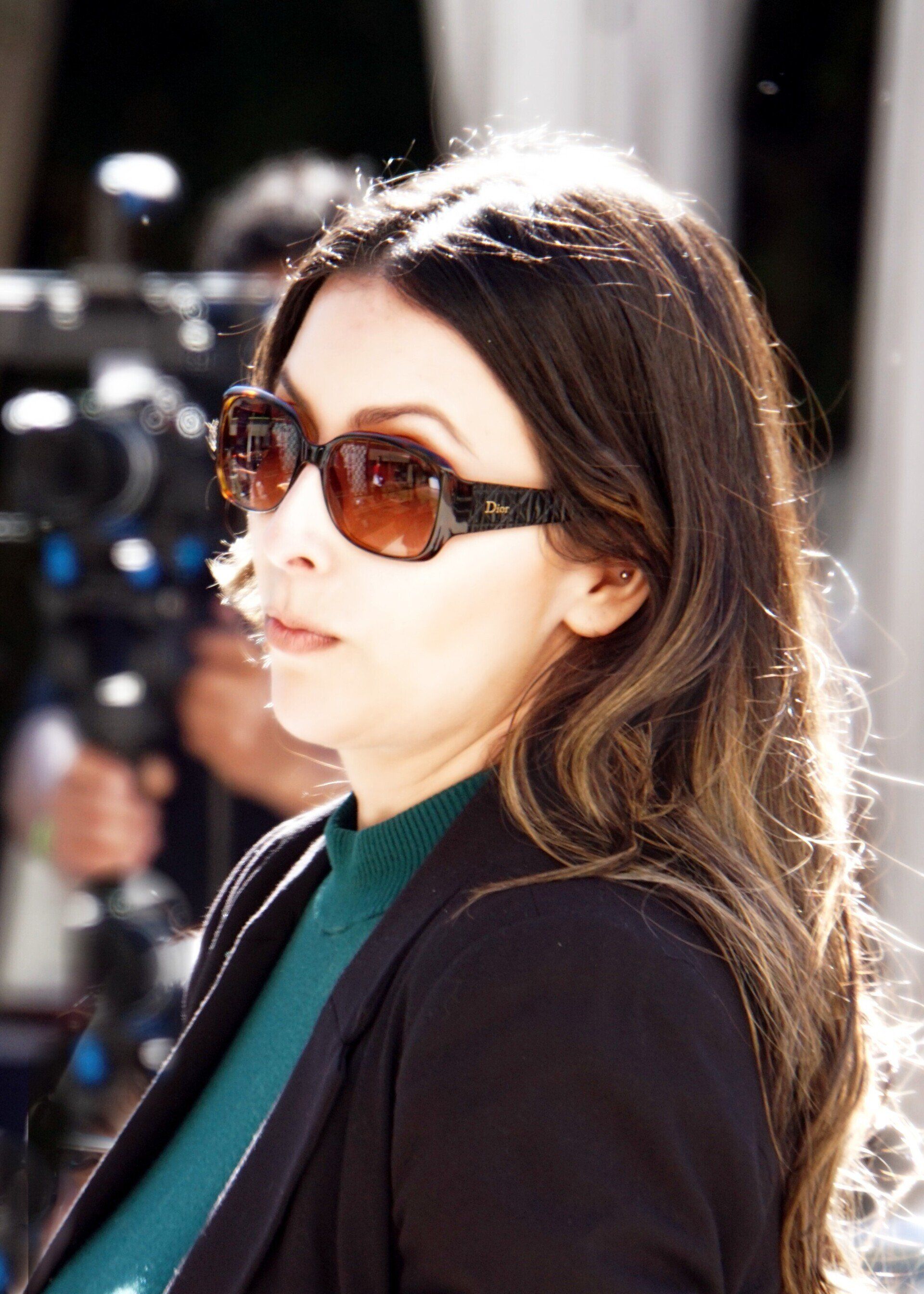 A woman wearing sunglasses is standing in front of a camera
