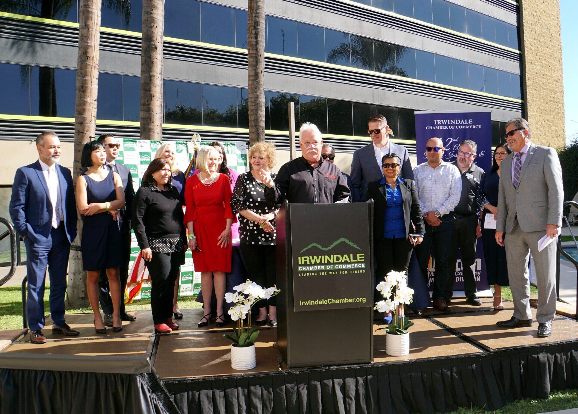 A group of people are standing around a podium with a building in the background.