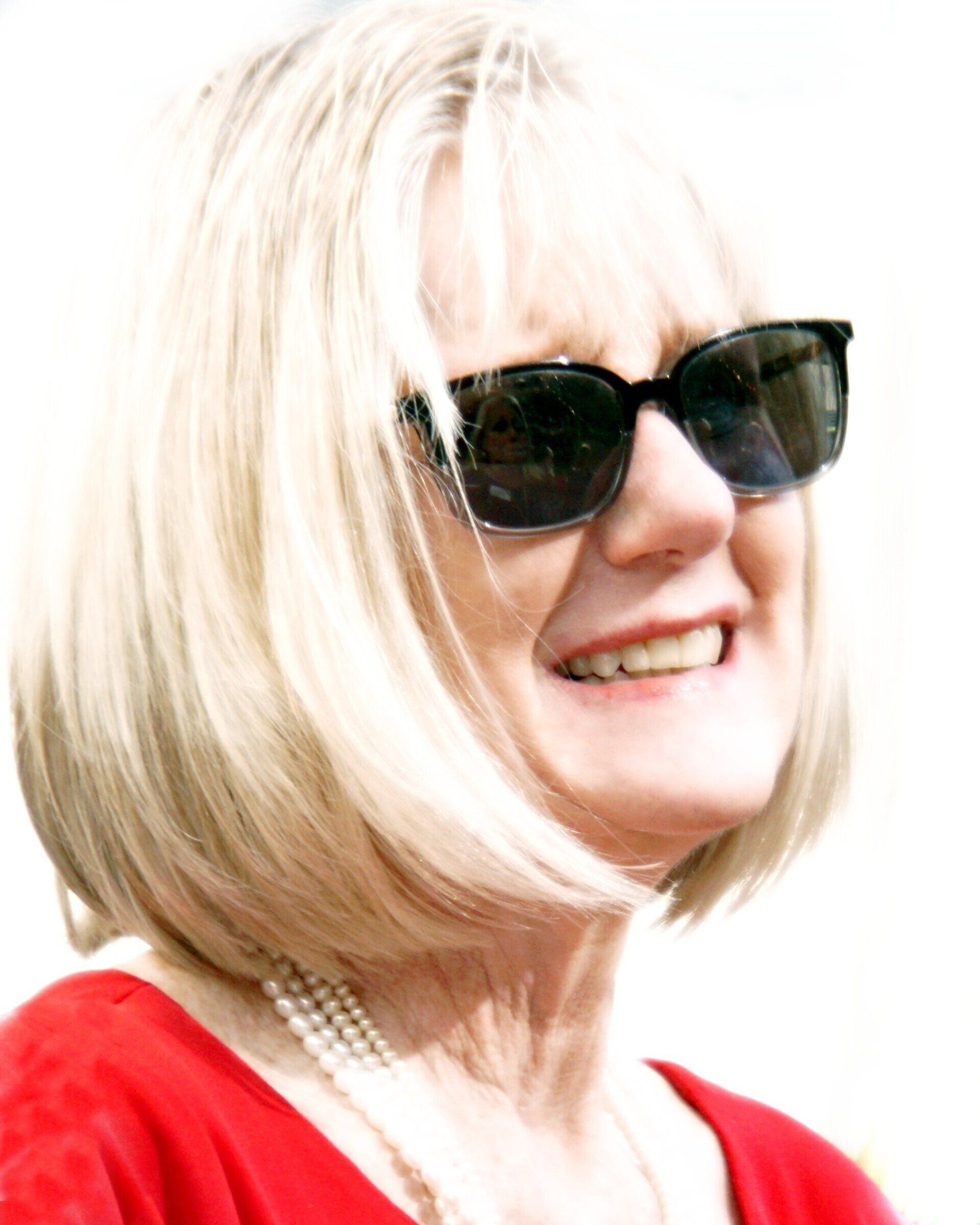A woman wearing sunglasses and a red shirt is smiling