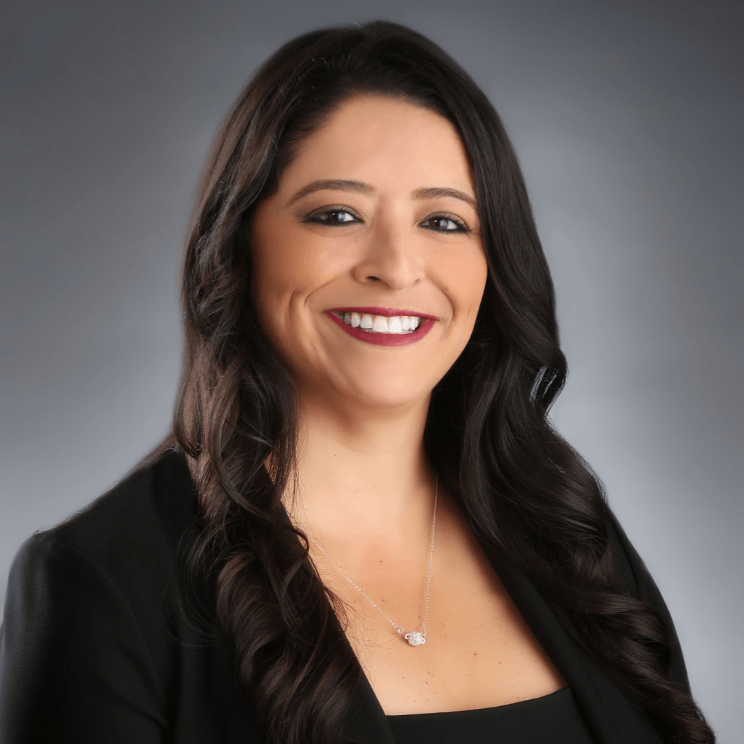 A woman wearing a black jacket and necklace smiles for the camera
