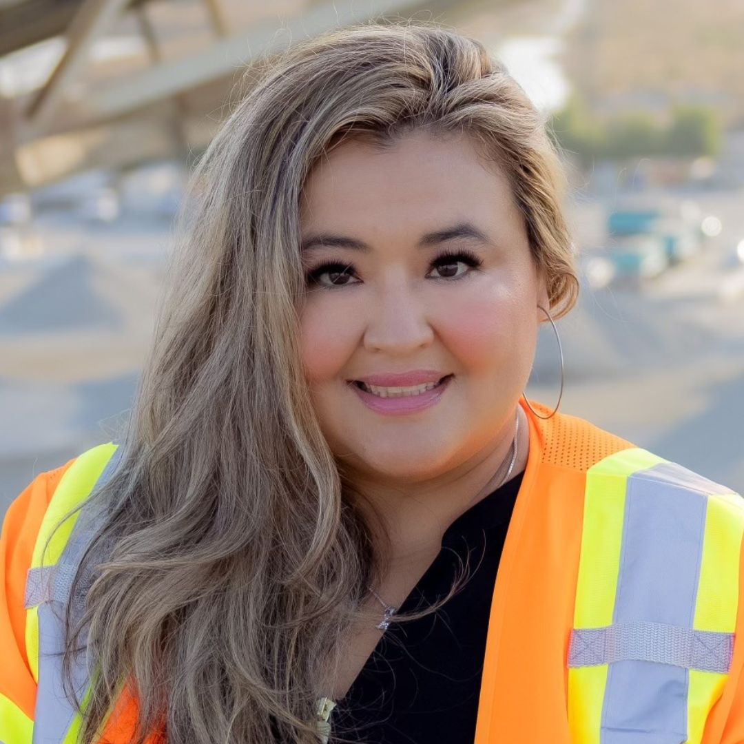 A woman wearing an orange and yellow safety vest smiles for the camera