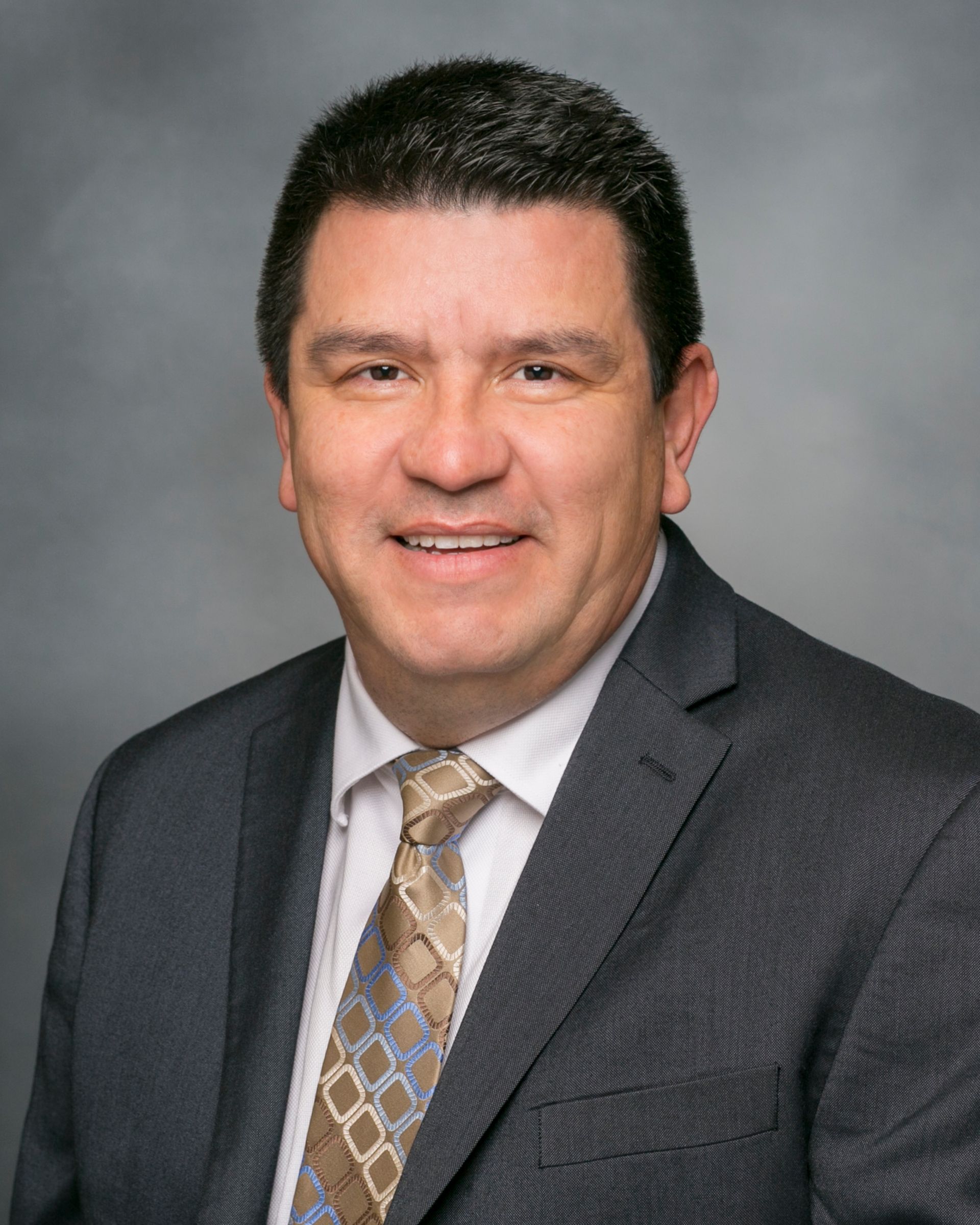 A woman wearing a green and white sweater and a pearl necklace smiles for the camera