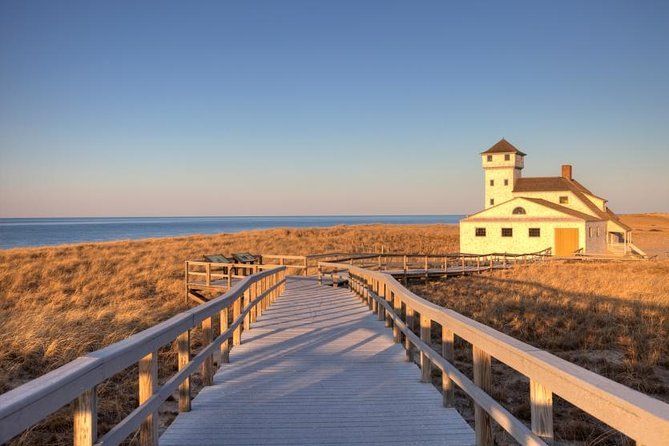 A wooden walkway leads to a white house on a hill overlooking the ocean.