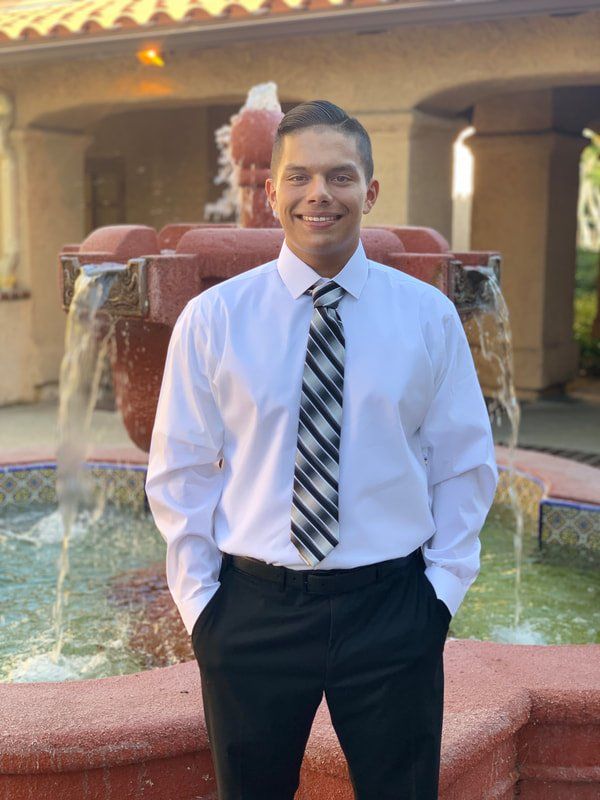 A man in a white shirt and tie is standing in front of a fountain.