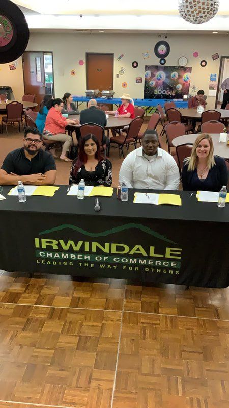 A group of people are sitting at a table with a sign that says irwindale chamber of commerce.