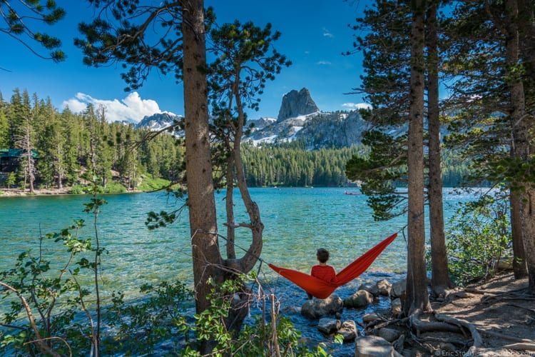 A person is sitting in a hammock on the shore of a lake.
