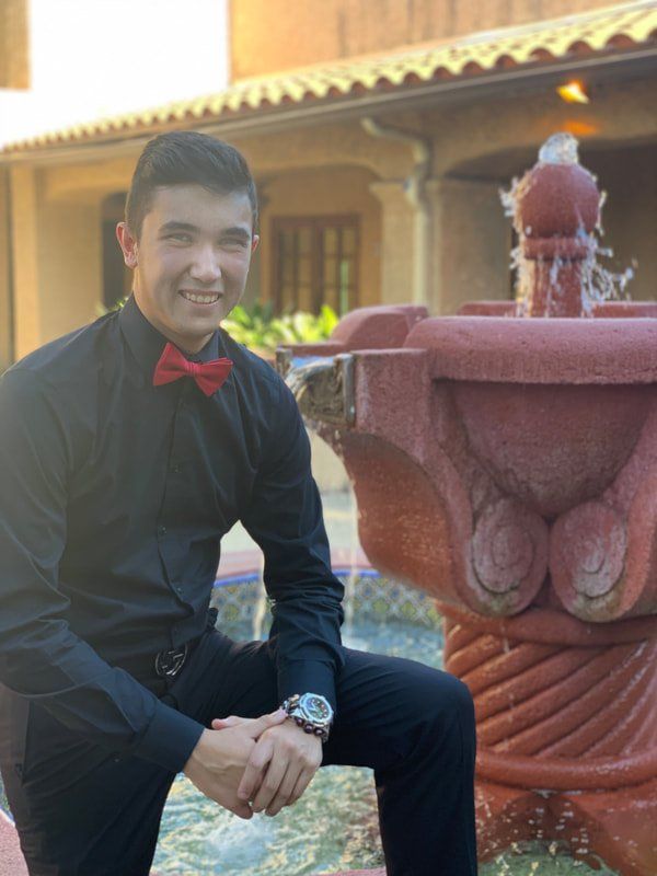 A man in a black shirt and red bow tie is sitting in front of a fountain.