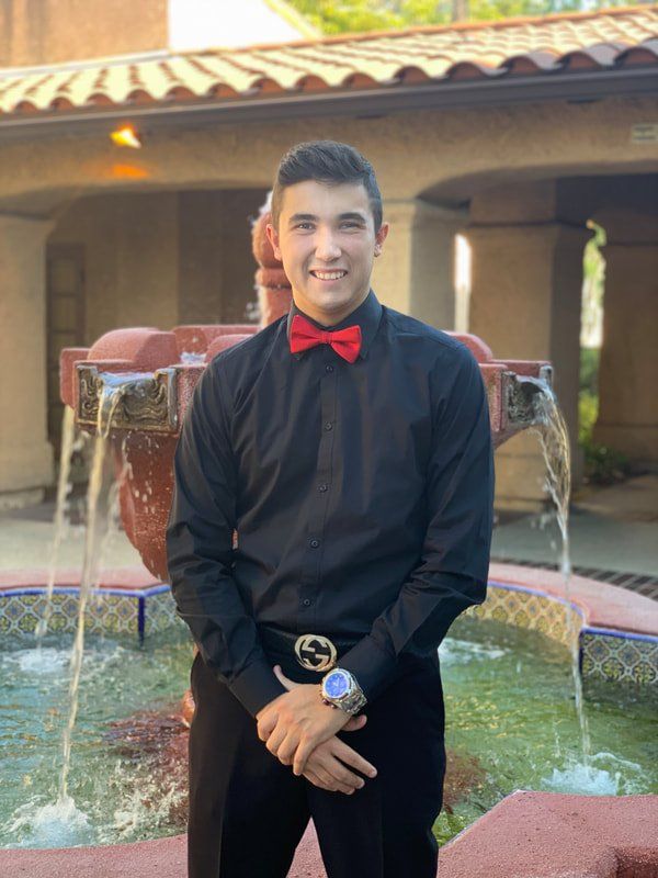 A man in a black shirt and red bow tie is standing in front of a fountain.