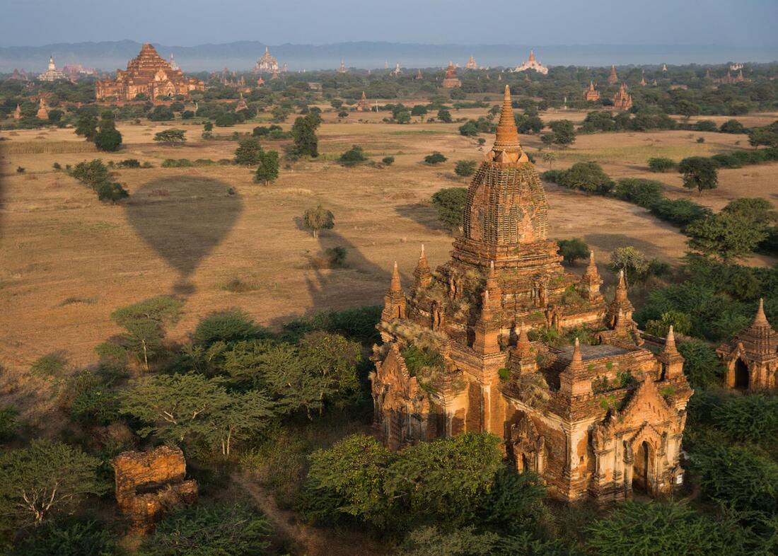 An aerial view of a temple with a hot air balloon casting a shadow on it.