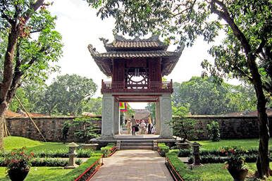 A group of people are standing in front of a pagoda in a park.