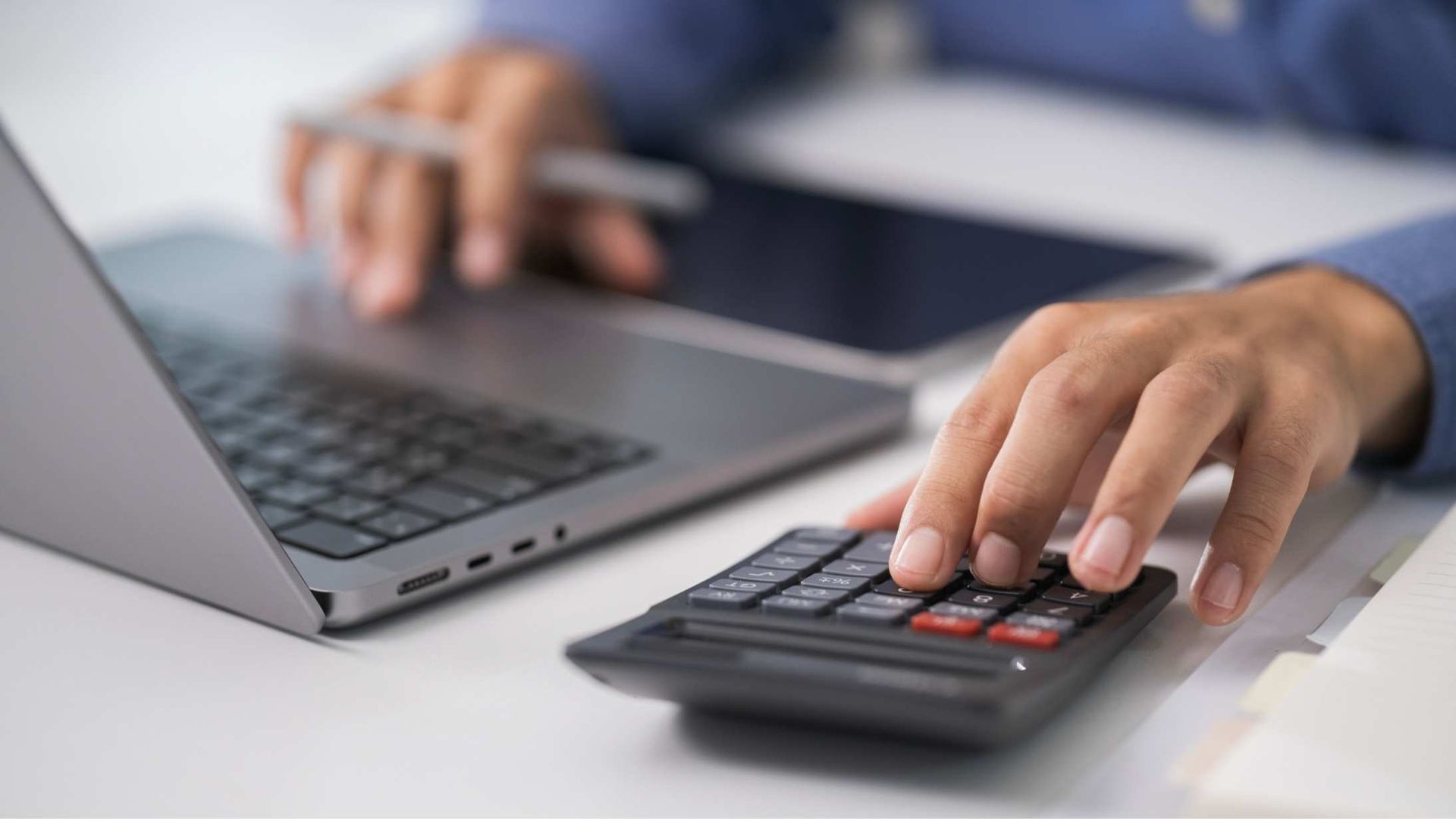 Hands using a laptop and calculator on a desk