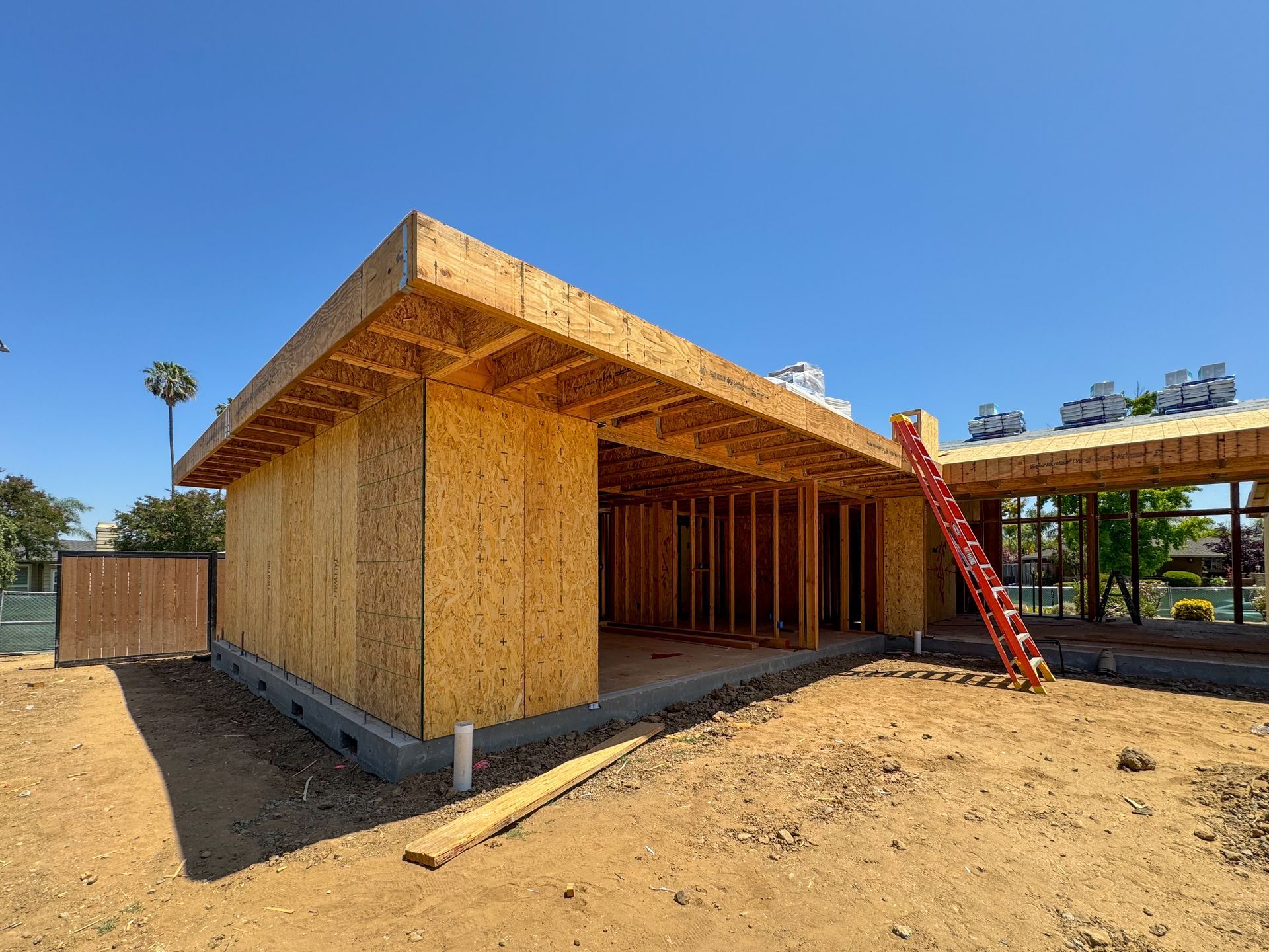 Construction site: Unfinished building with wood frame, walls, and roof against a blue sky. Ladder leaning against the side.