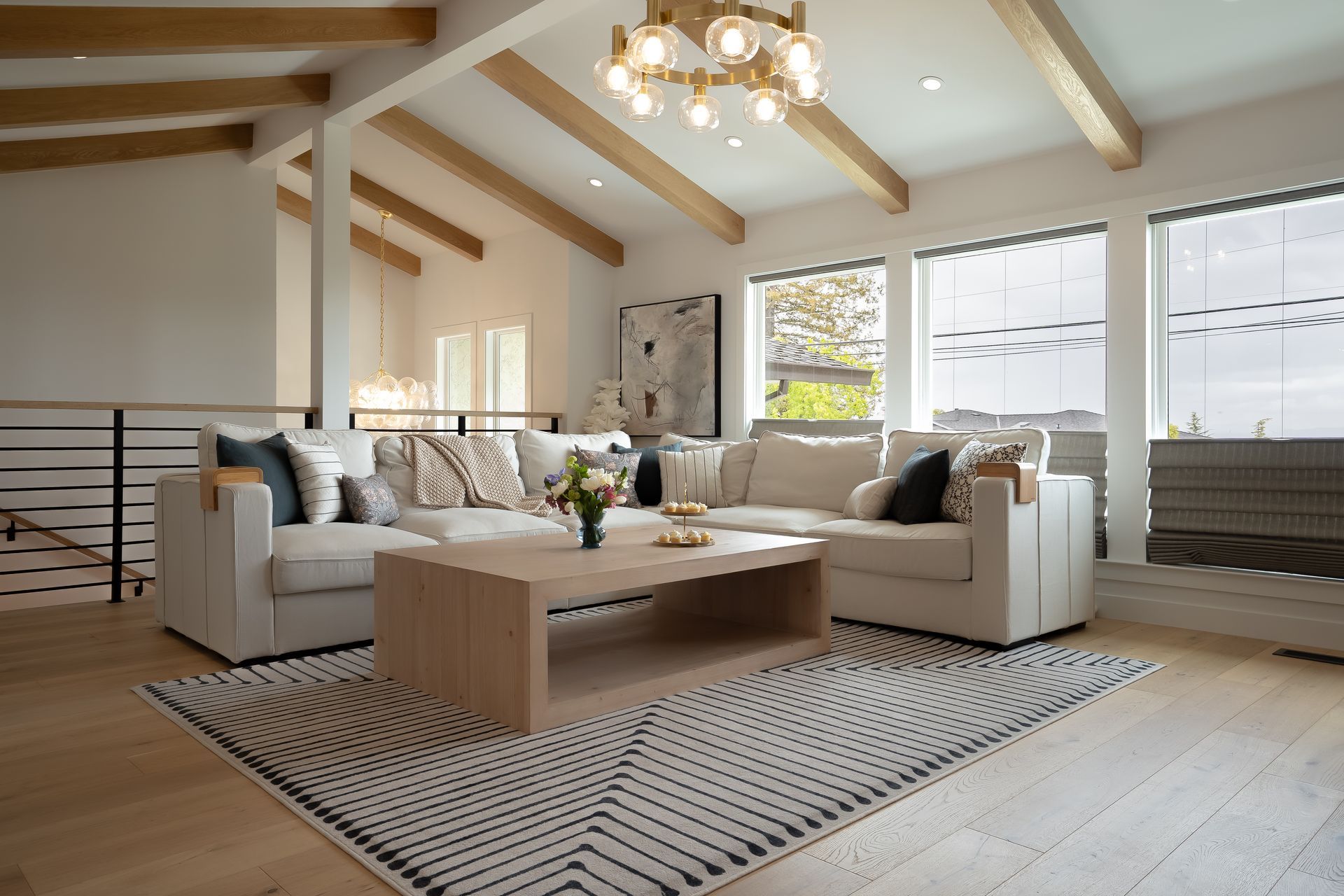 Modern living room with white sectional, wooden beams, and large windows.