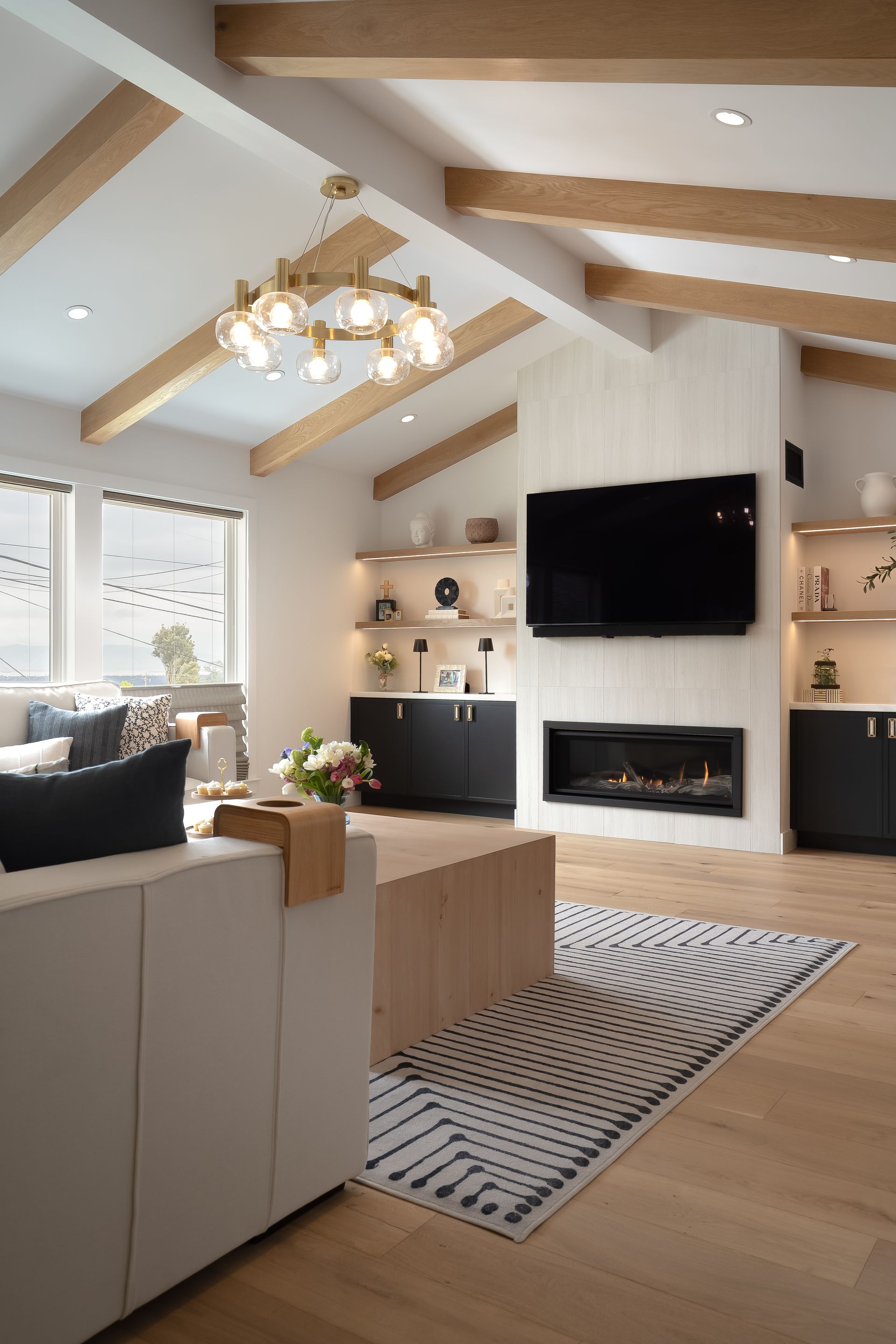 Living room with vaulted ceiling, fireplace, TV, and rug; neutral tones with wooden beams.