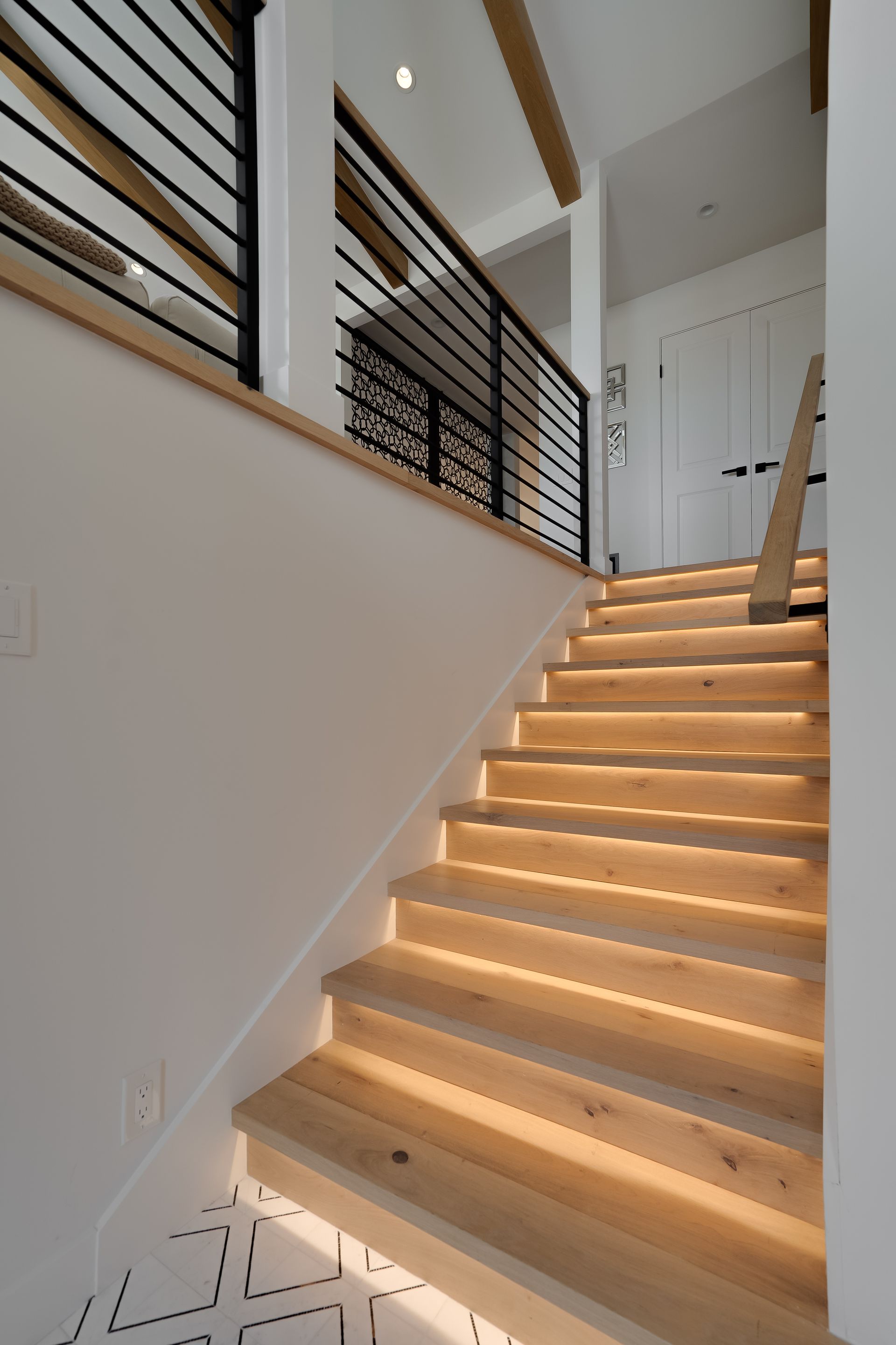 Wooden staircase with built-in lighting. Black railing and white walls.
