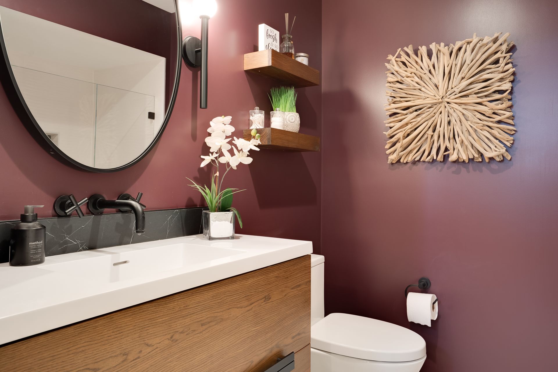 Modern bathroom with a burgundy wall, round mirror, and white countertop and sink.