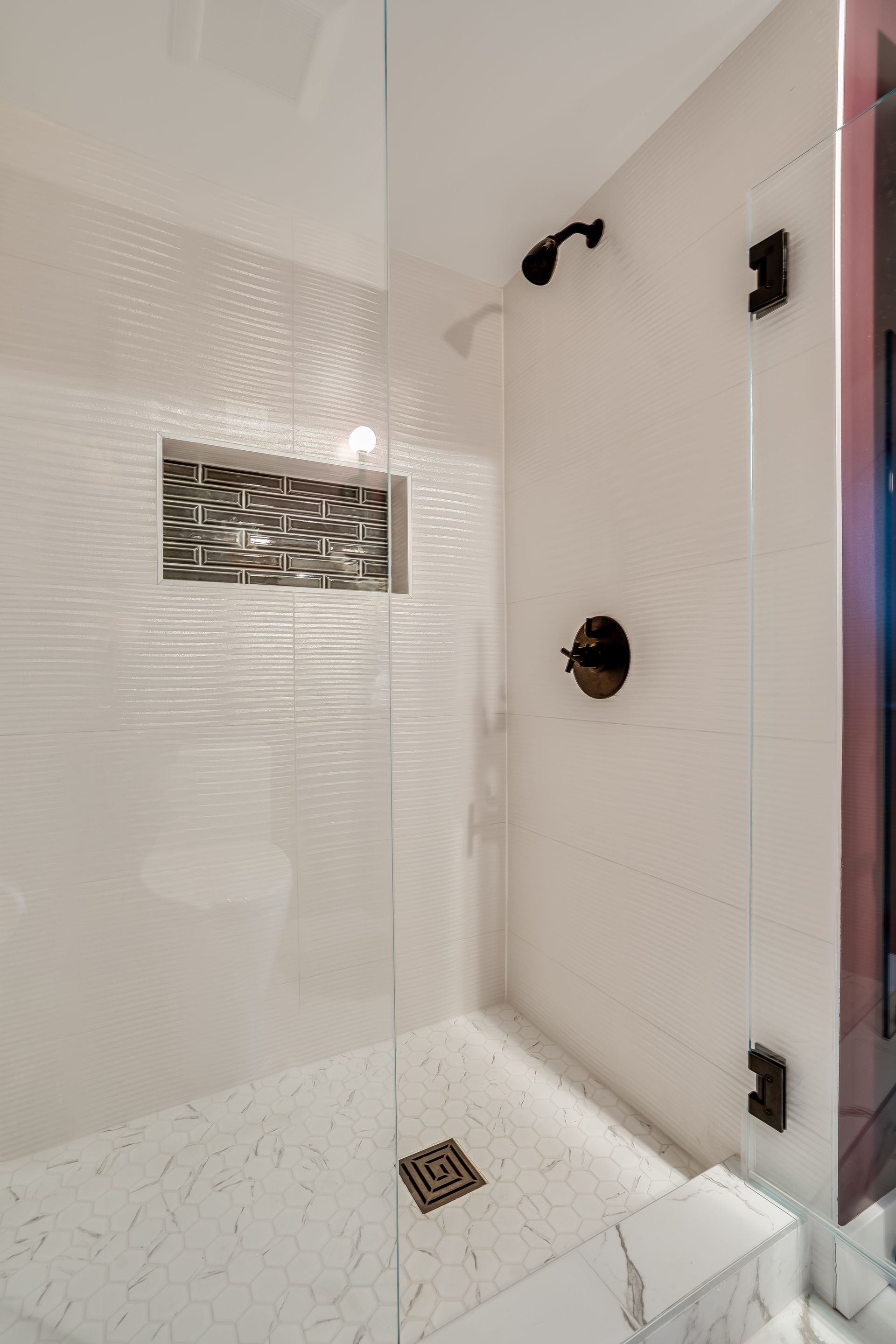 Modern white shower with glass door, textured wall, marble floor, and black fixtures.