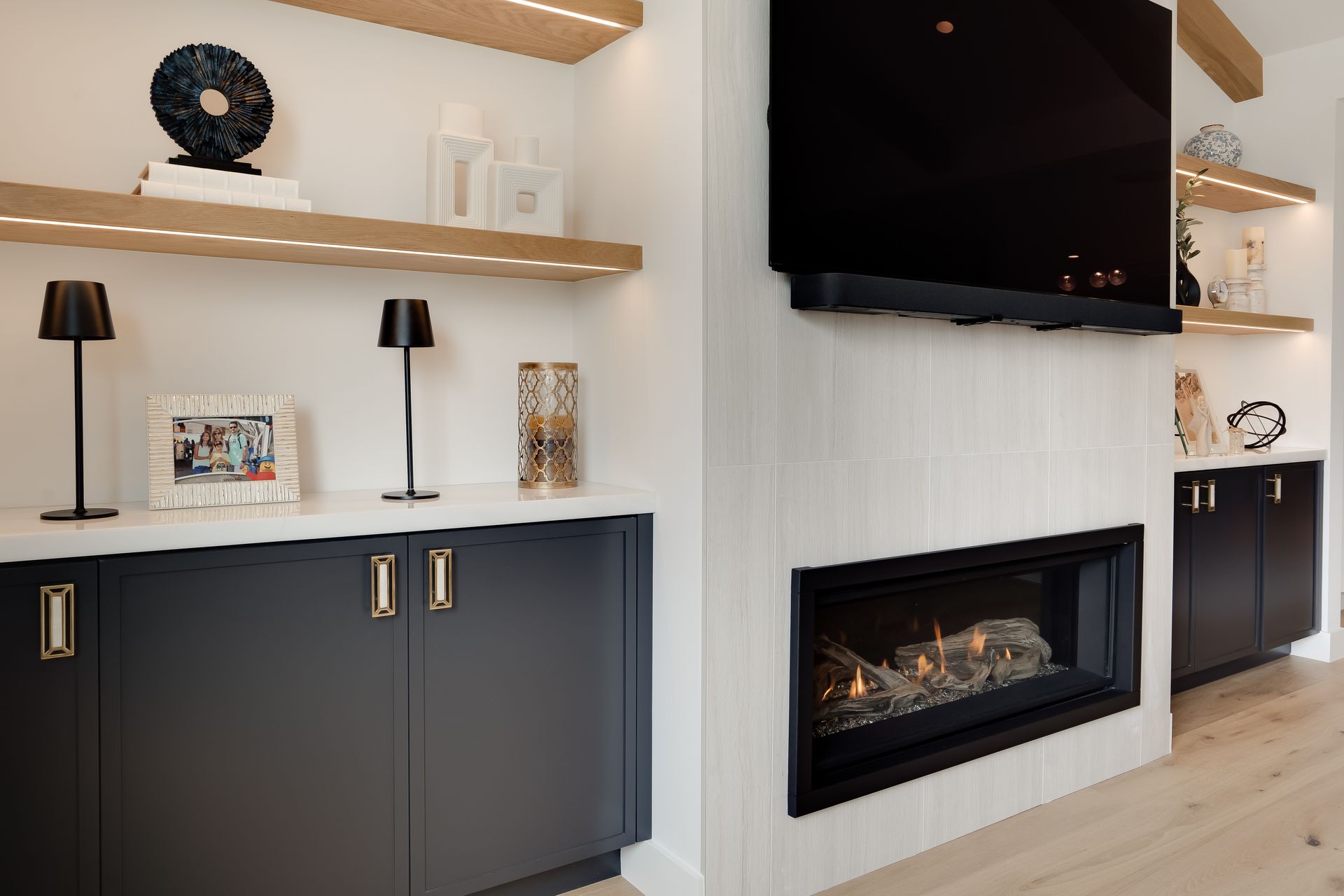 Modern living room with fireplace, TV, built-in shelves, navy cabinets, and light-colored wood accents.