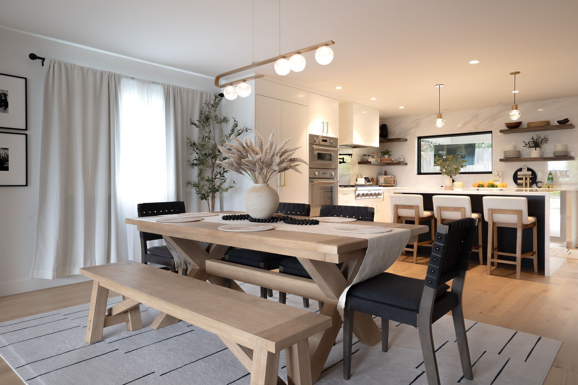 Dining room with a large wooden table, bench, and chairs, open to a kitchen with a breakfast bar.