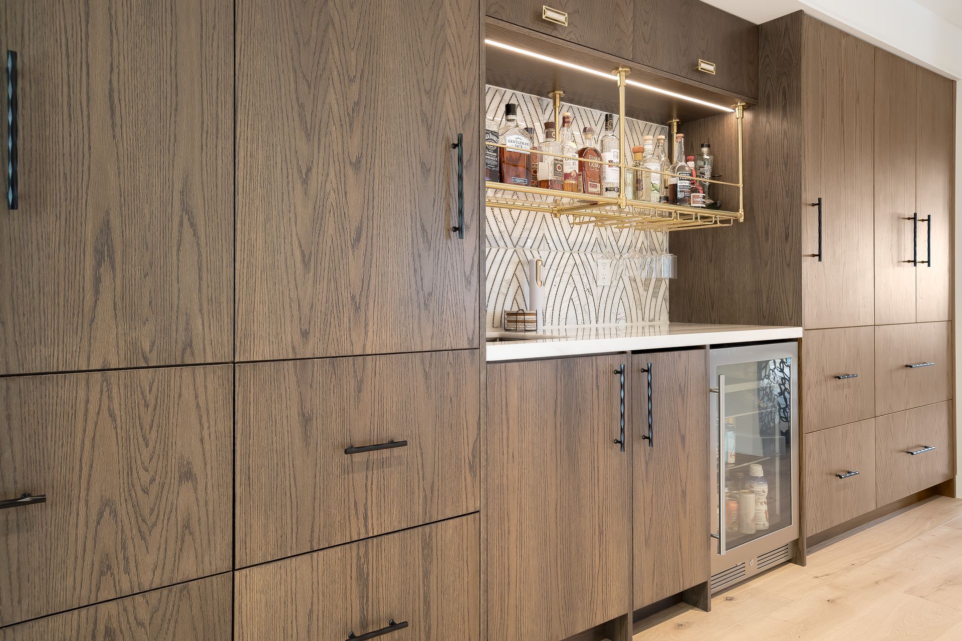 Wooden home bar with cabinets, shelves holding liquor, and a mini-fridge.