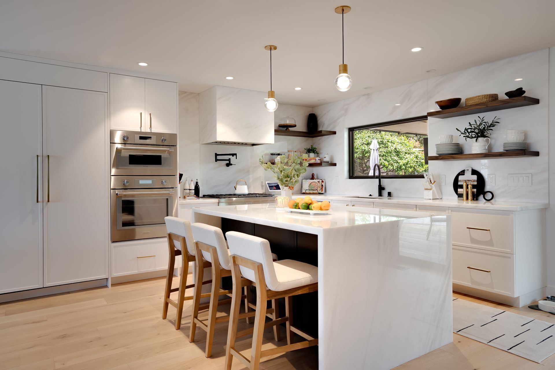 Modern white kitchen with island, bar stools, and stainless steel appliances.