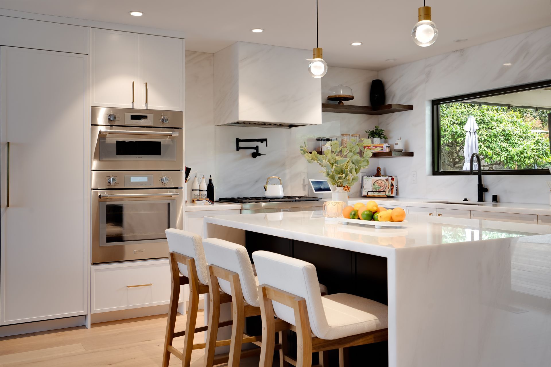 Modern kitchen with white cabinets, island with bar stools, stainless steel appliances, and a window.