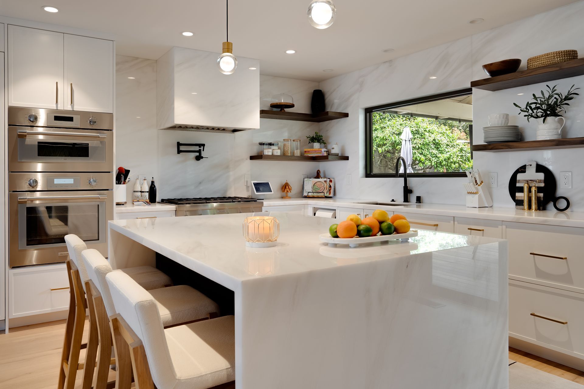 Modern white kitchen with island, stainless steel appliances, and wooden shelves.