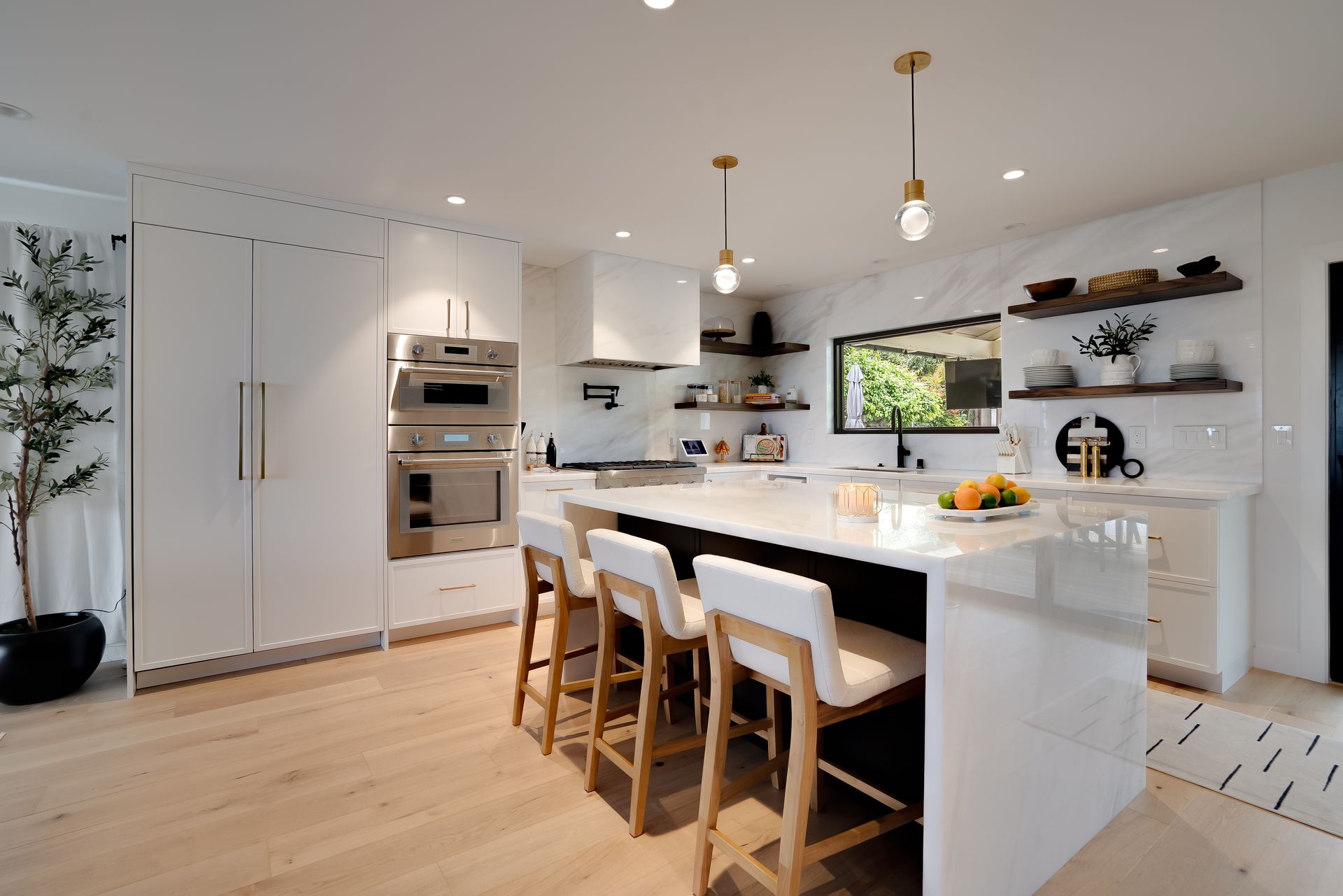 Modern white kitchen with island, light wood floor, and marble backsplash; bar stools at island.