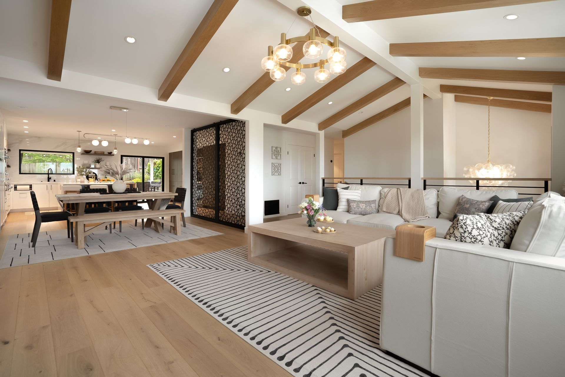 Living room with light wood floors, vaulted ceiling with beams, and modern furniture.