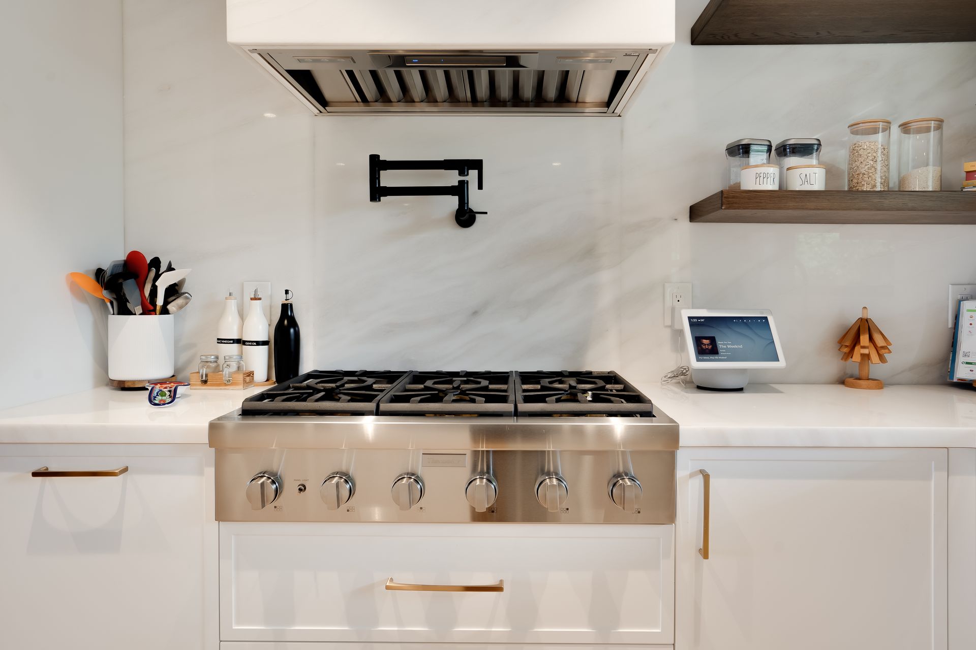 Stainless steel range in white kitchen with marble backsplash, pot filler, and open shelving.