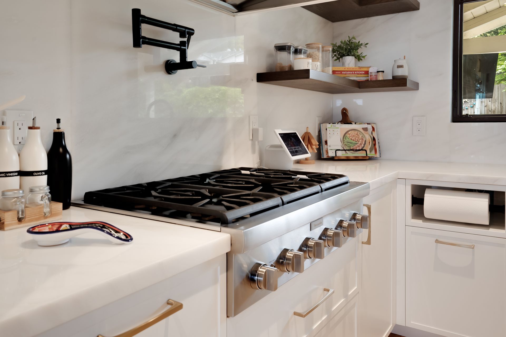 Modern kitchen with gas range, white cabinets, marble backsplash, and open shelving.