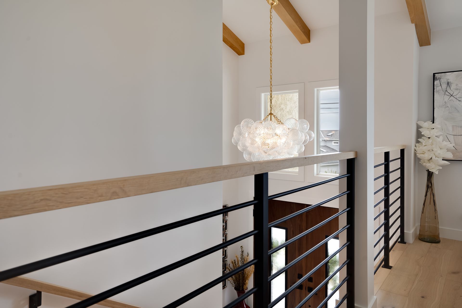 A bright, modern hallway with a chandelier and black railing.