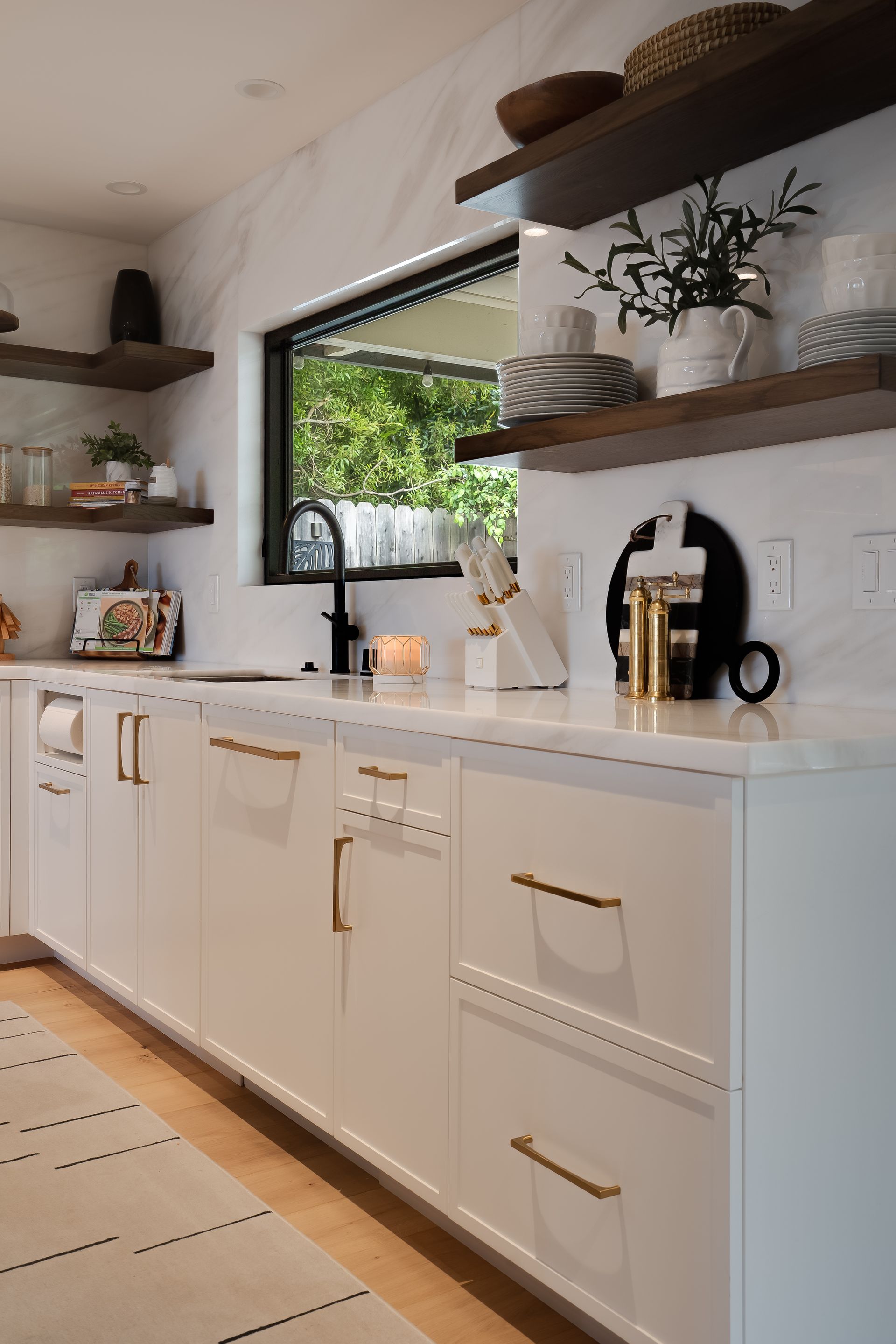 Modern white kitchen with gold hardware and open shelving.