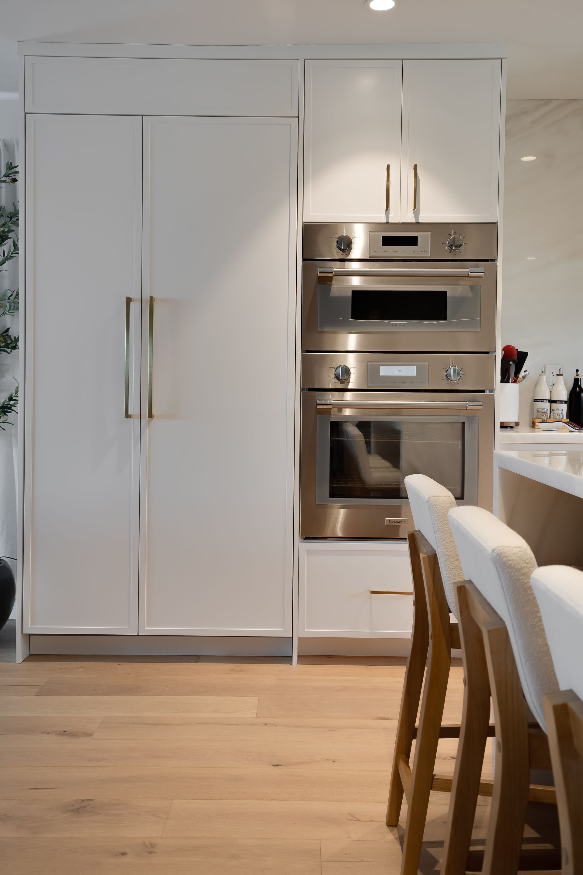 White kitchen cabinets with stainless steel appliances, and wood bar stools.