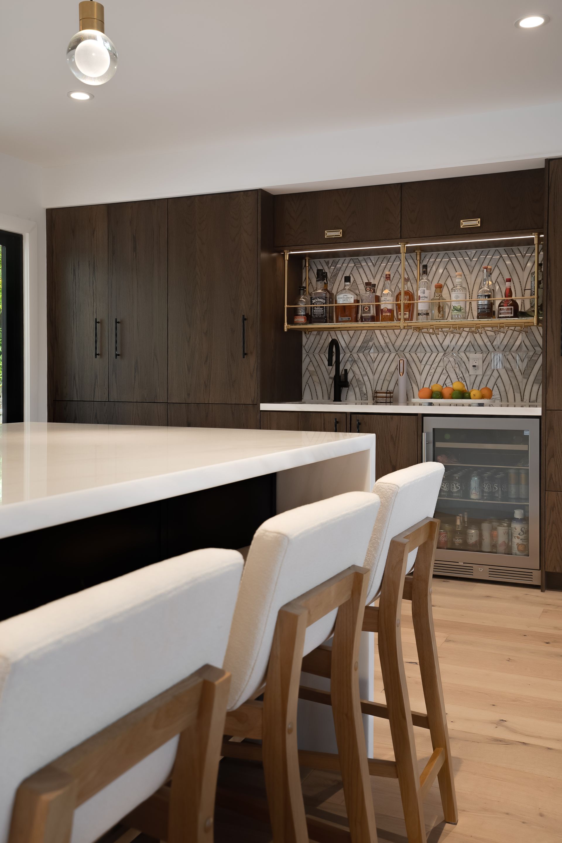 Modern kitchen with a white countertop island, dark wood cabinets, and a bar area. Three white bar stools.