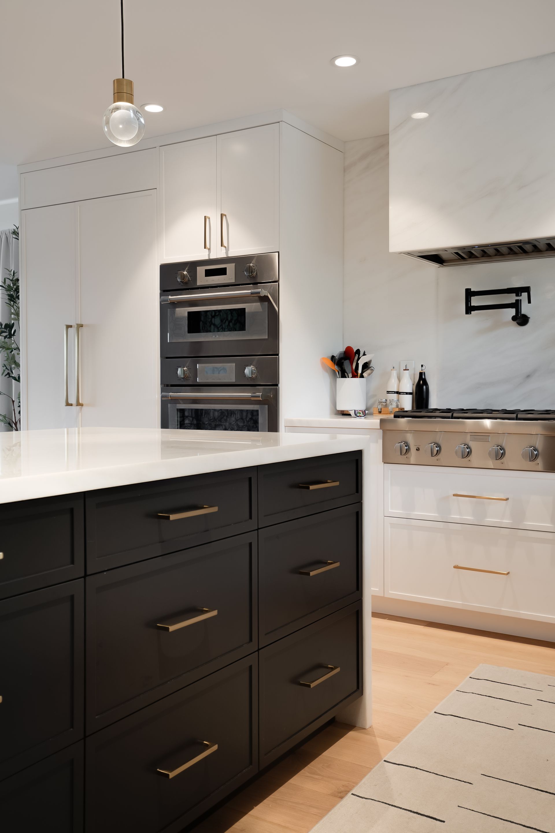 Modern kitchen with black island, white countertops, stainless steel appliances, and gold accents.