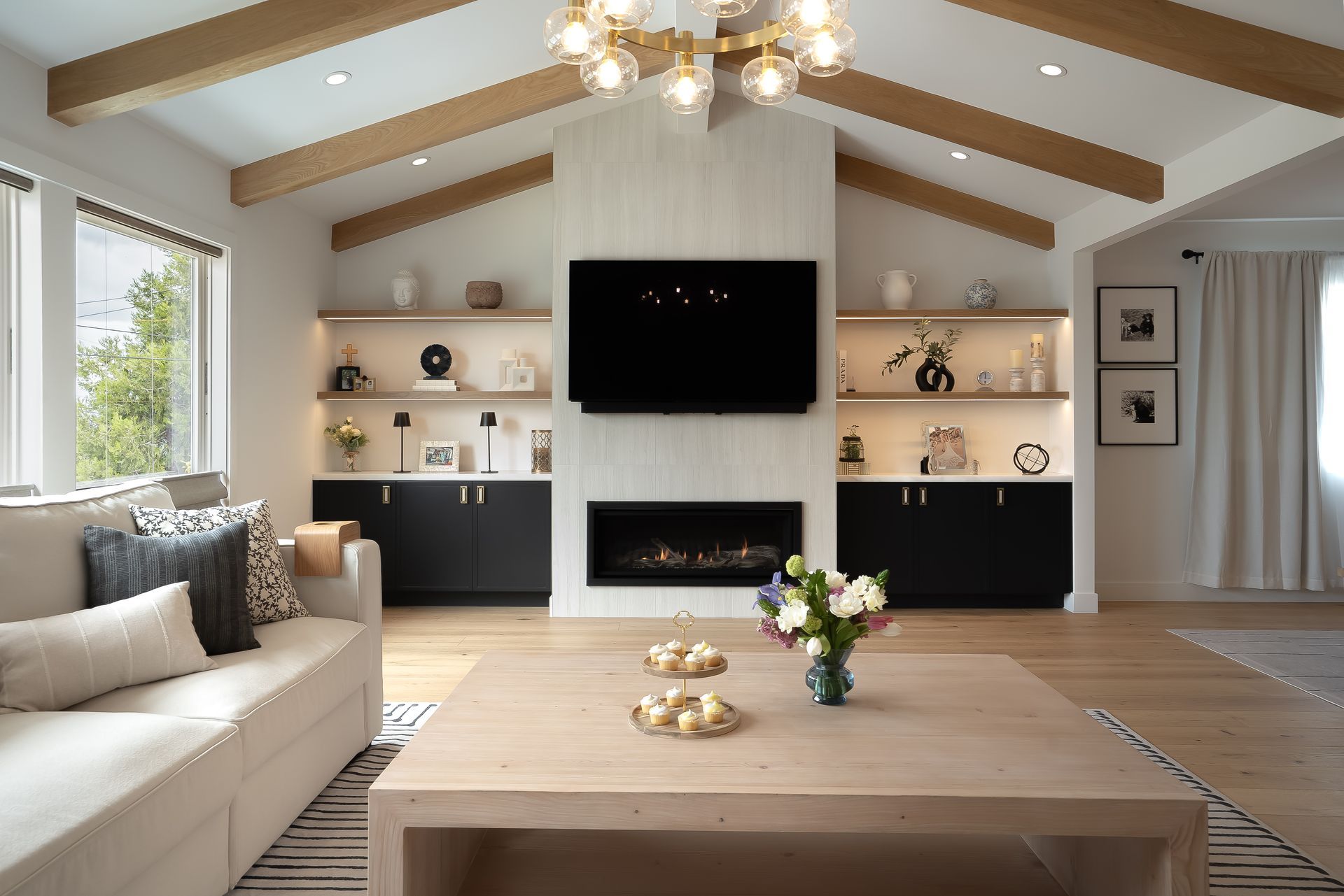 Living room with fireplace, built-ins, TV, and sofa. Light wood floors, white walls, and a neutral color palette.