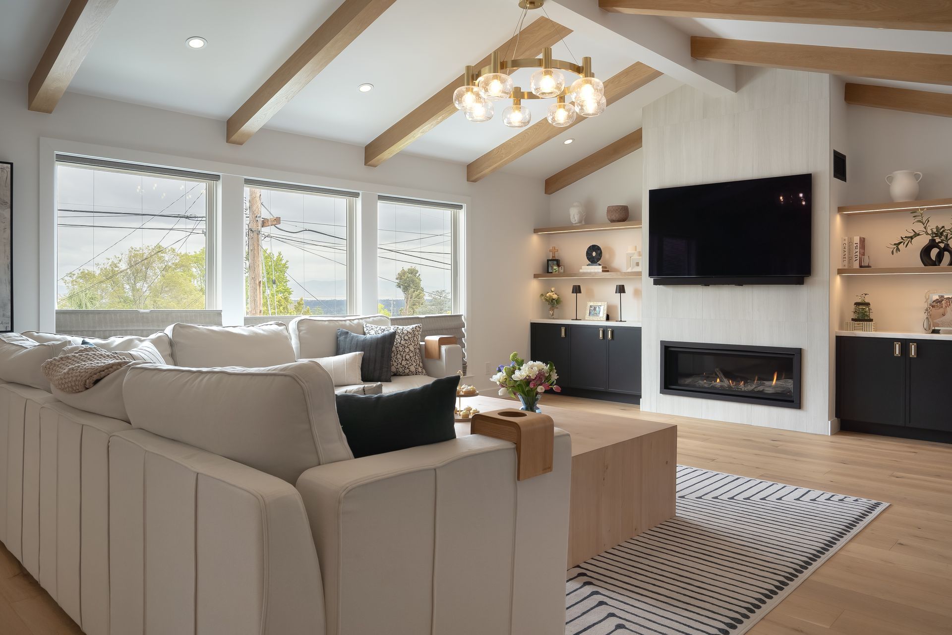 Modern living room with a large white sectional, fireplace, and light wood accents.