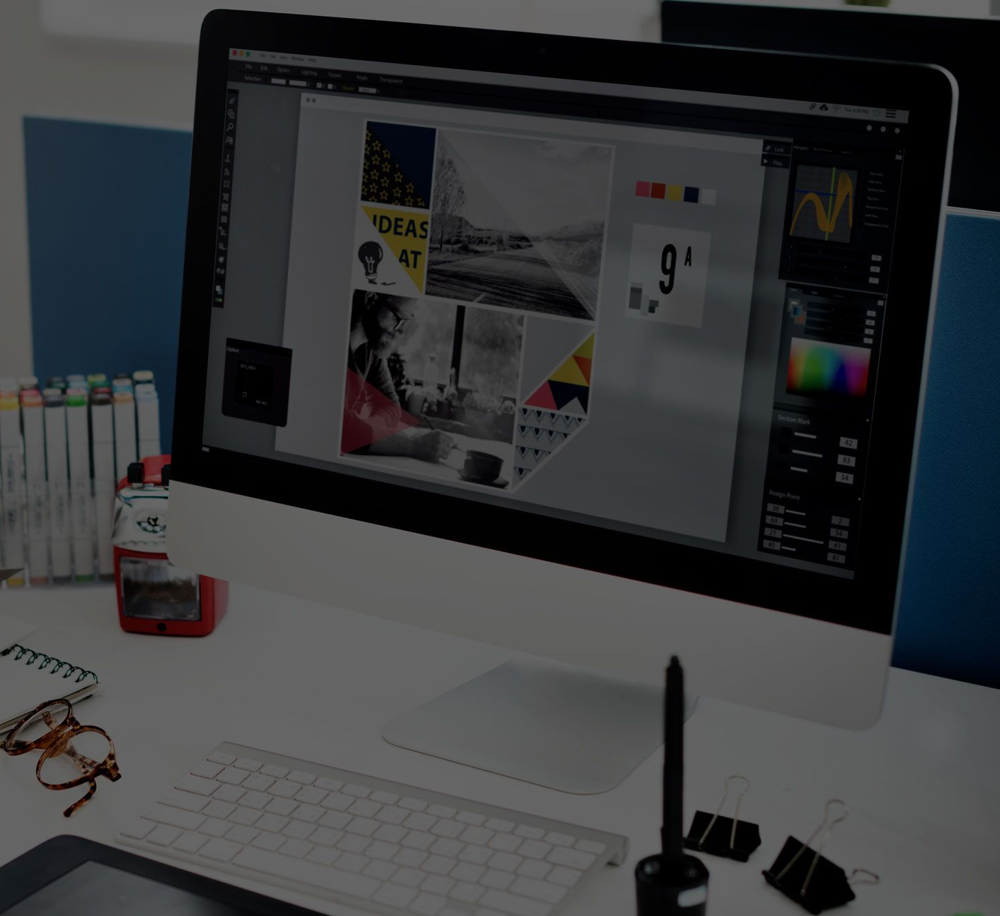 Desktop computer displaying design work, with a keyboard, pens, and paper on a desk.