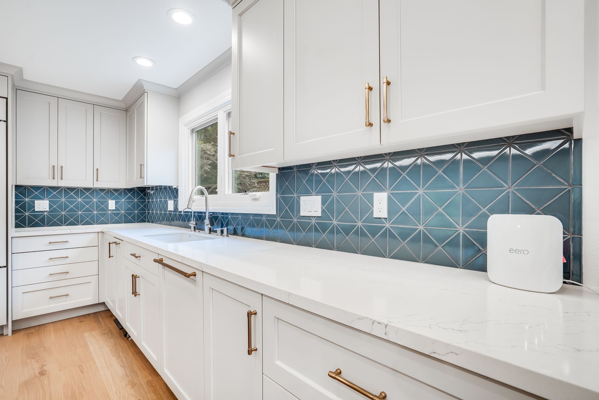 White kitchen with blue tile backsplash, gold hardware, and light wood floors.