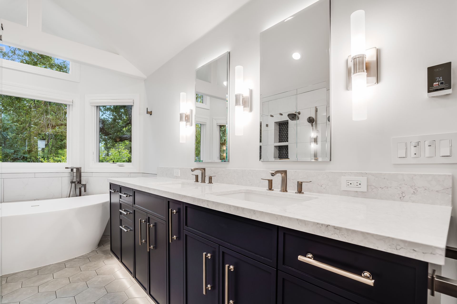 Modern bathroom with dark blue vanity, white countertop, mirrors, and a soaking tub.