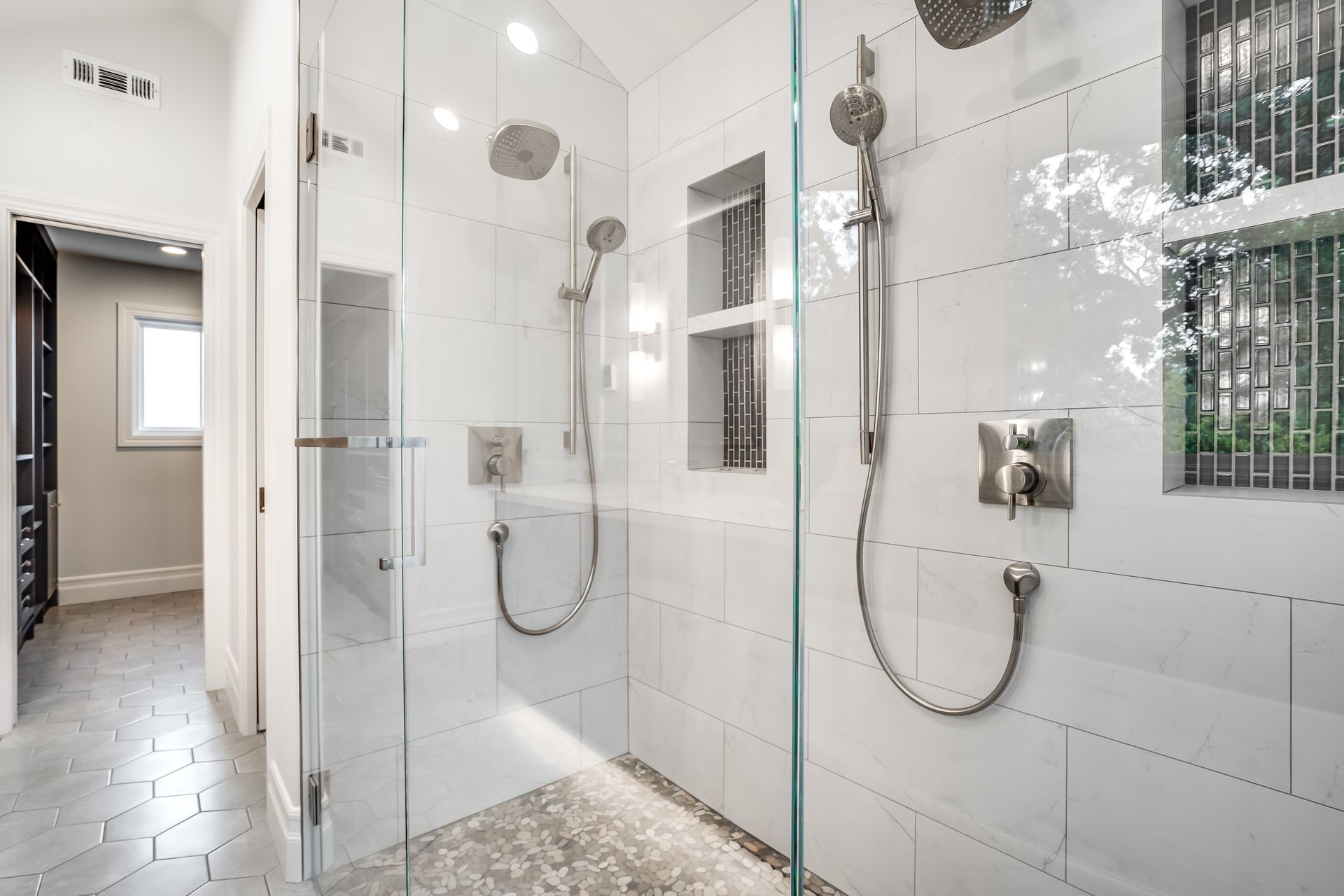 A modern bathroom with two showers, white tile walls, and glass doors.