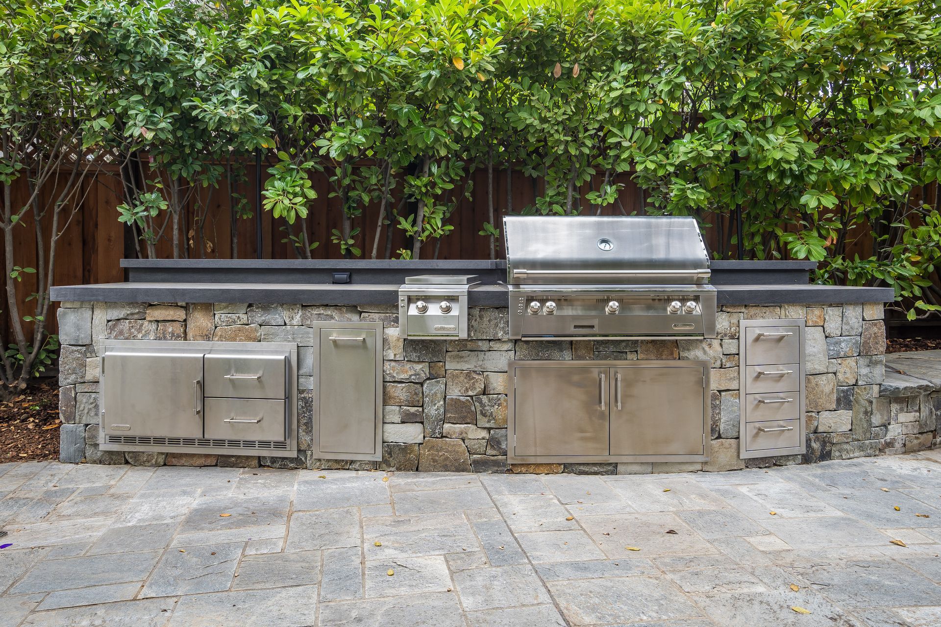 Outdoor kitchen with stone facade, stainless steel grill, and storage cabinets.