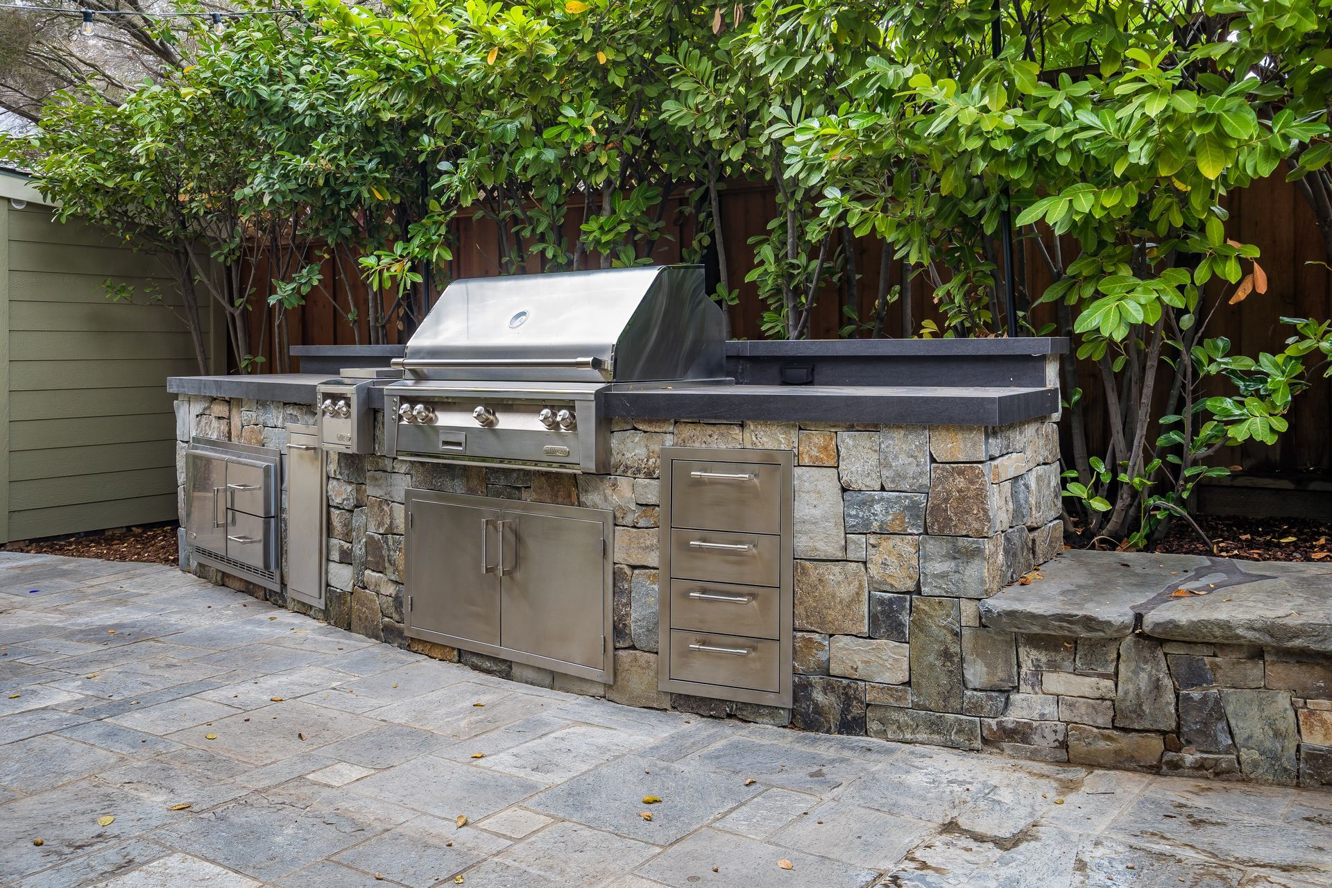 Outdoor kitchen with stainless steel grill and stone facade on a paved patio.