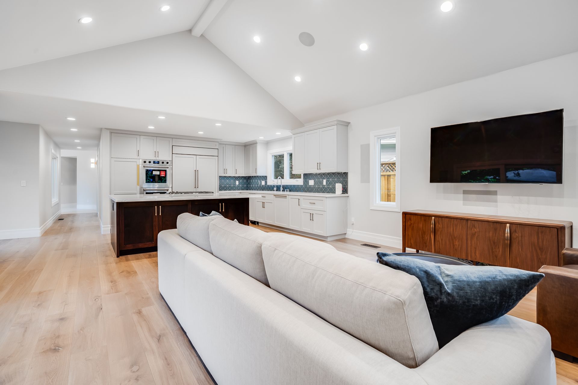Open-concept living space with kitchen, living area, white walls, light wood floors, and a dark wood island.