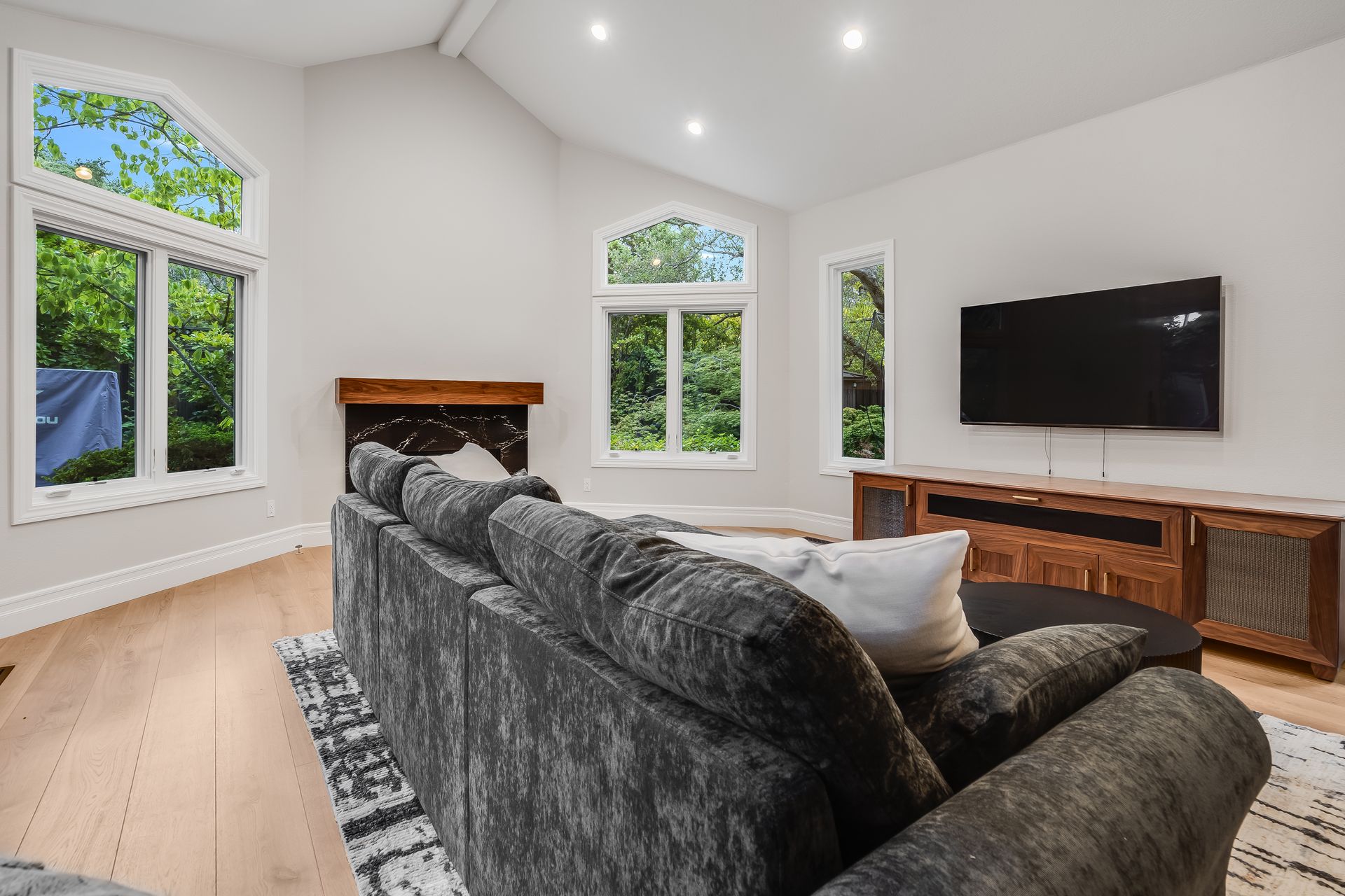 Cozy living room with gray couch, large windows, fireplace, and TV.