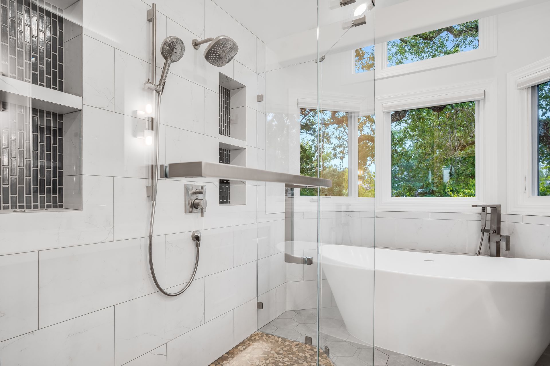 Bright white bathroom with a walk-in shower, soaking tub, and windows overlooking trees.